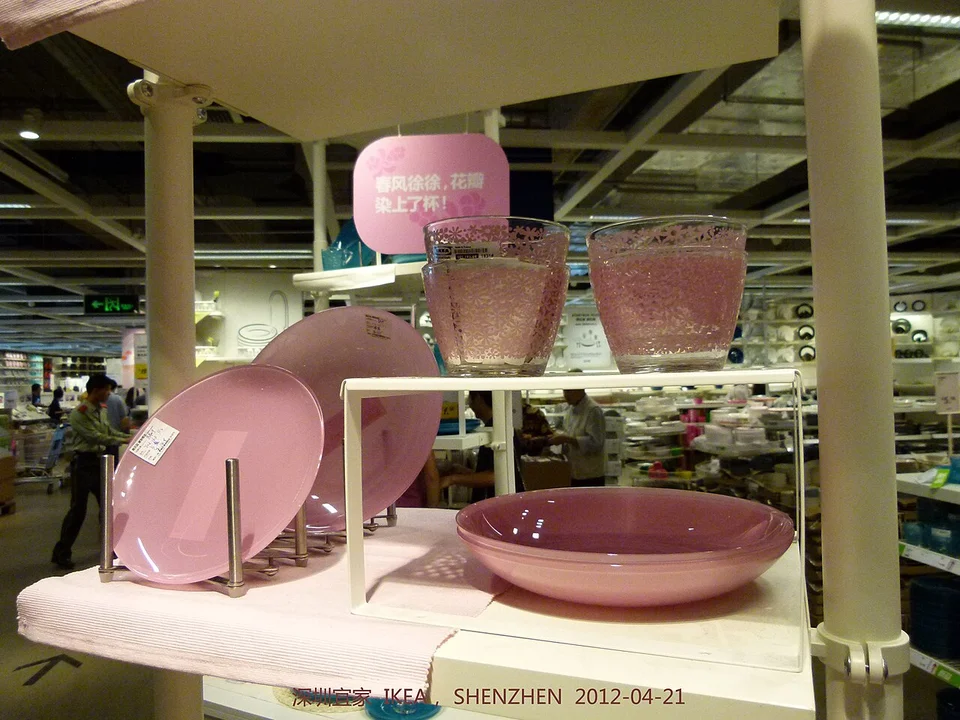 Upright pink plates in a metal plate holder beside a shelf insert in an IKEA display