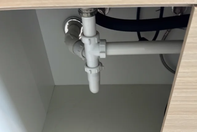 White plumbing pipes occupying space inside an under-sink cabinet